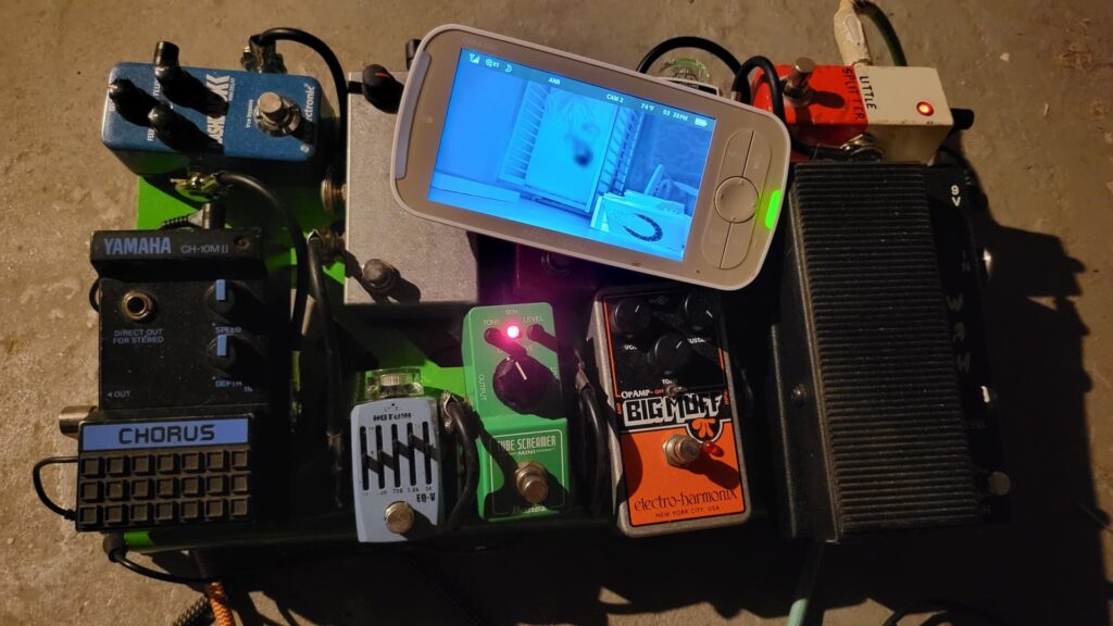 picture of a guitar pedalboard with a baby monitor on it showing a toddler who won't sleep